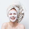 Image of woman smiling wearing a facial mask and towel on her head